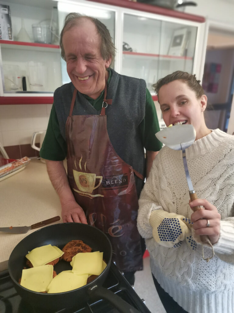 A man and a woman wearing aprons at the stove cooking veggie burgers