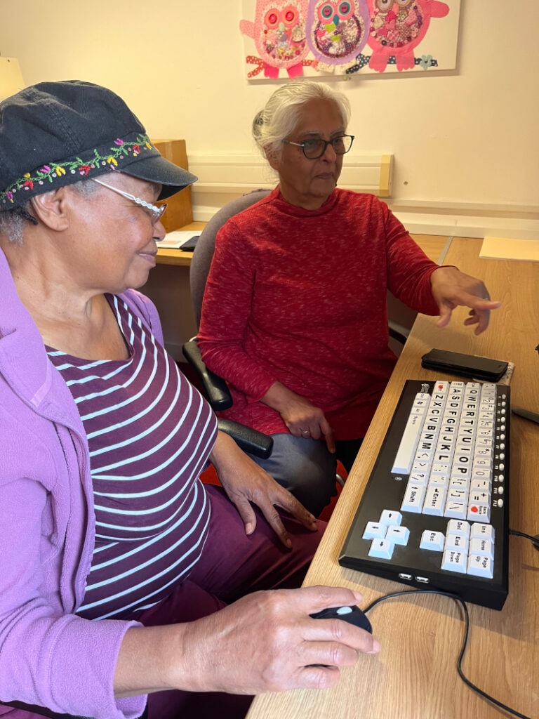 A partially sighted woman being supported by a volunteer to use a PC with a large button keyboard