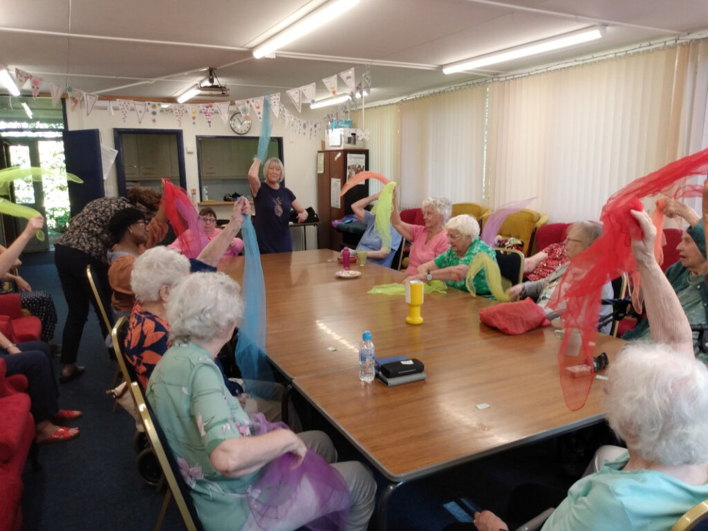 A woman leading members of the Monday Club in armchair exercises