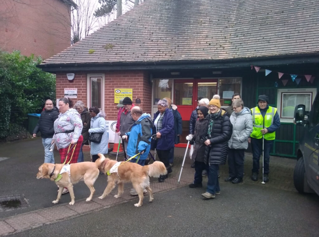 A group of 15 visually impaired people and sighted guides with two guide dogs setting off on a walk